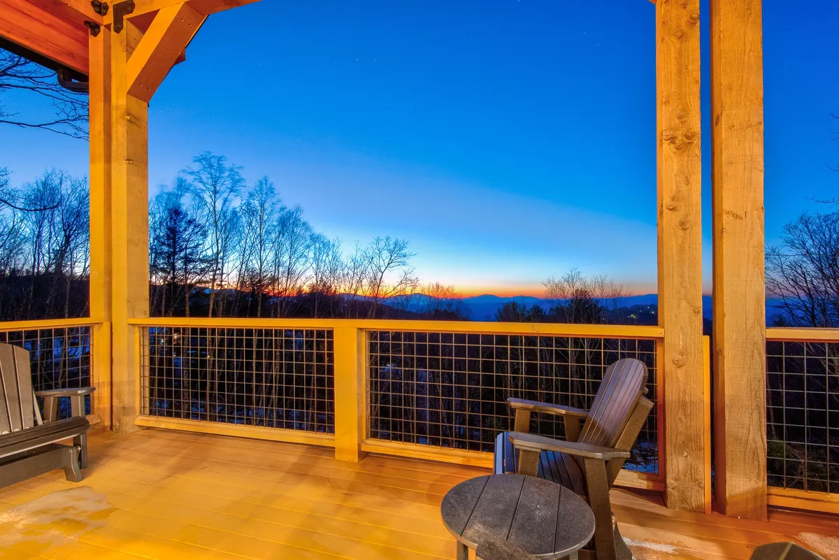 A tranquil deck area offers panoramic mountain views beneath a colorful sunset sky. The space is perfect for morning coffee, quiet contemplation, or evening stargazing, surrounded by the gentle sounds of nature.