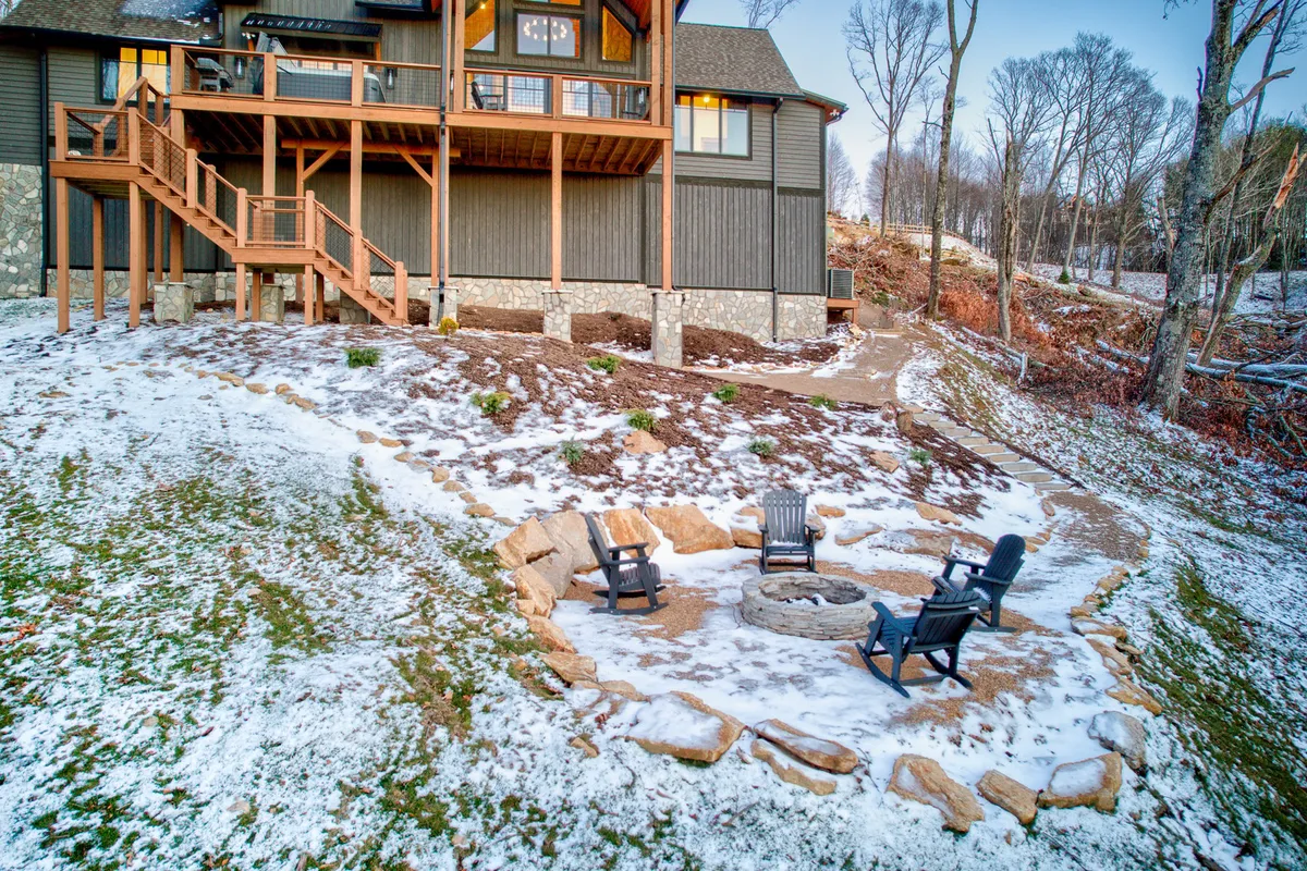 A cozy exterior view of the house, highlighting a large balcony, a welcoming fire pit area with seating, and a snow-covered landscape. The fire pit hints at group gatherings, while the balcony and snowy ground reinforce year-round adventure, from winter fun to summer evenings outdoors.