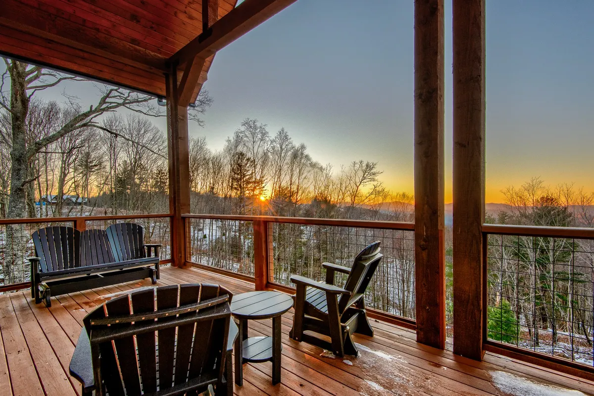 A wooden deck equipped with classic Adirondack chairs overlooks a sweeping sunset view. The scene captures a warm, inviting atmosphere for families and friends to relax together while surrounded by nature. The golden sky adds a magical touch and hints at memorable evenings spent outdoors.