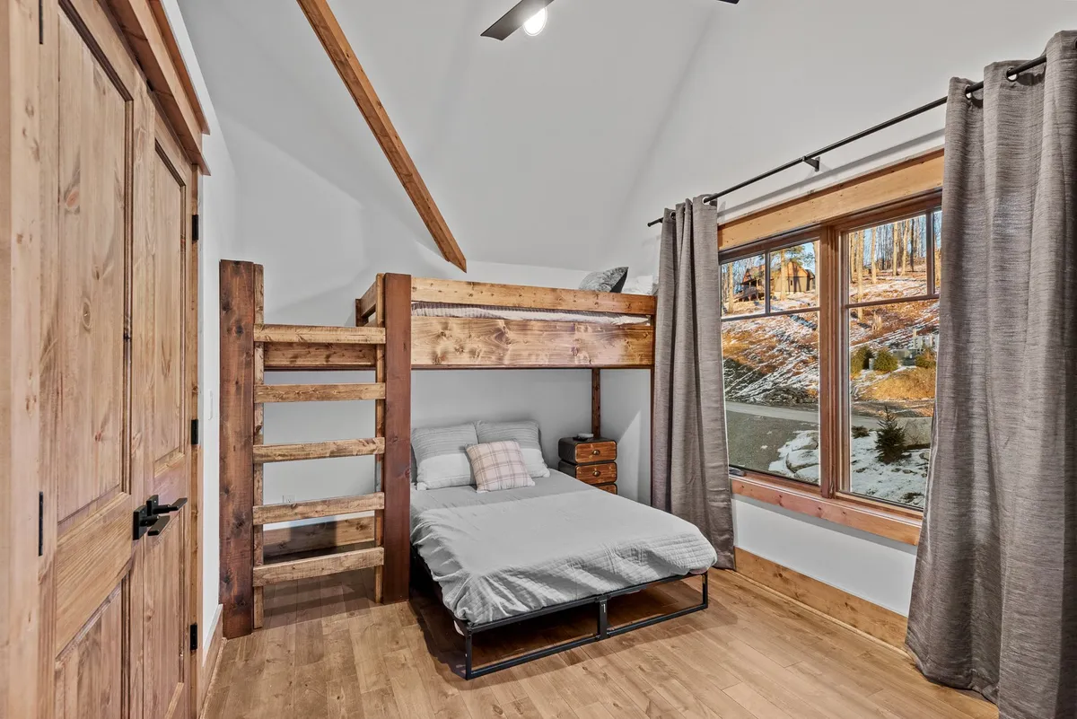 A playful, welcoming bunk room with a twin-over-full bunk bed, a large window letting in light, and a wooden door. The space is perfect for children or friends, with a cozy reading nook by the window.